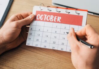 Cropped view of man holding pen and calendar with october month near laptop on table