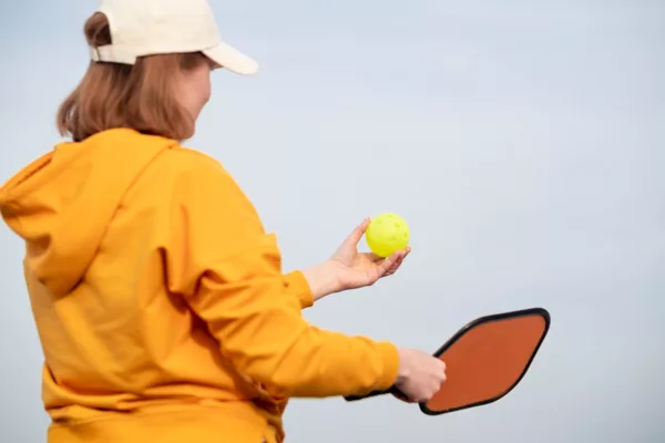Back View Pickleball Game Woman Player, Hands Over Blue Sky Hitting Pickleball Yellow Ball With Paddle, Outdoor Sport Leisure Activity.